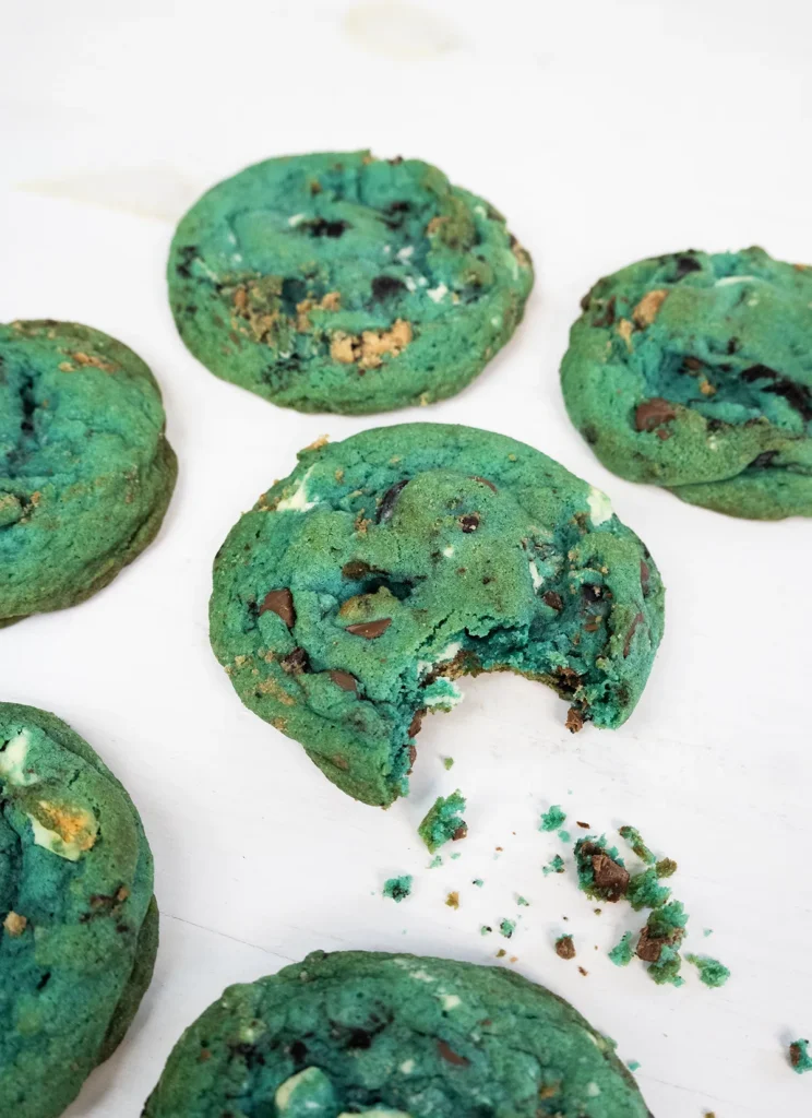 Blue cookie monster cookies on a white background. One cookie has a bite taken out of it with some crumbs.