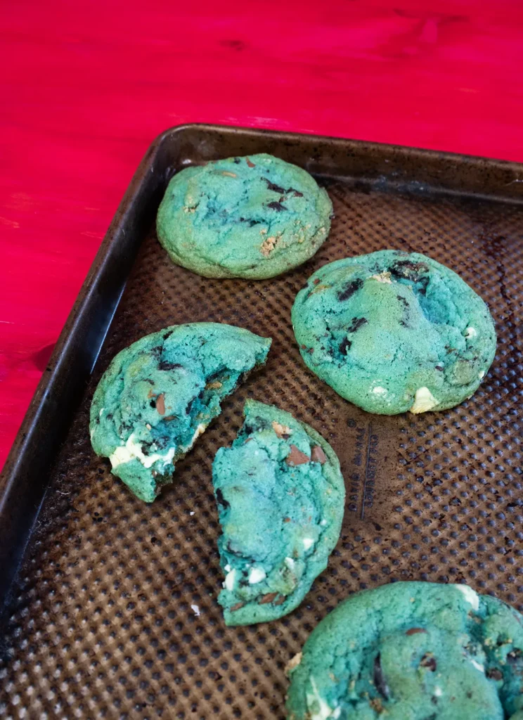 Blue cookie monster cookies arranged on a baking sheet. One is broken in half.