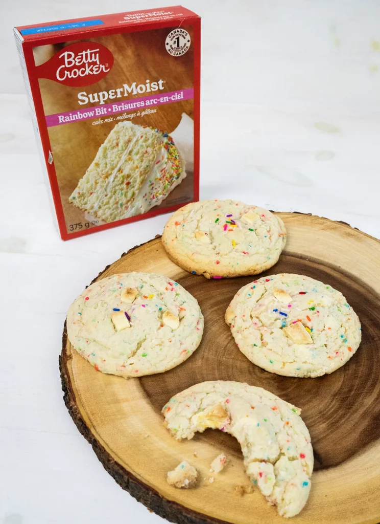 Funfetti cake mix cookies arranged on a wooden plate, with a box of cake mix in the background.