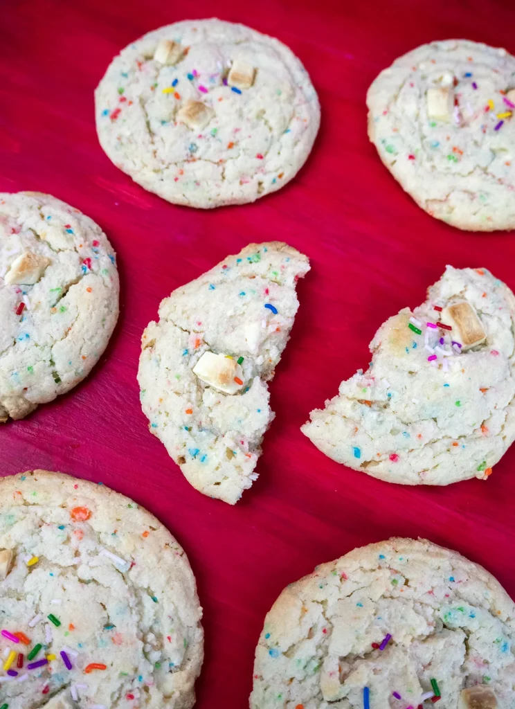 Funfetti cake mix cookies arranged on a pink wooden surface. One cookie is broken in half.