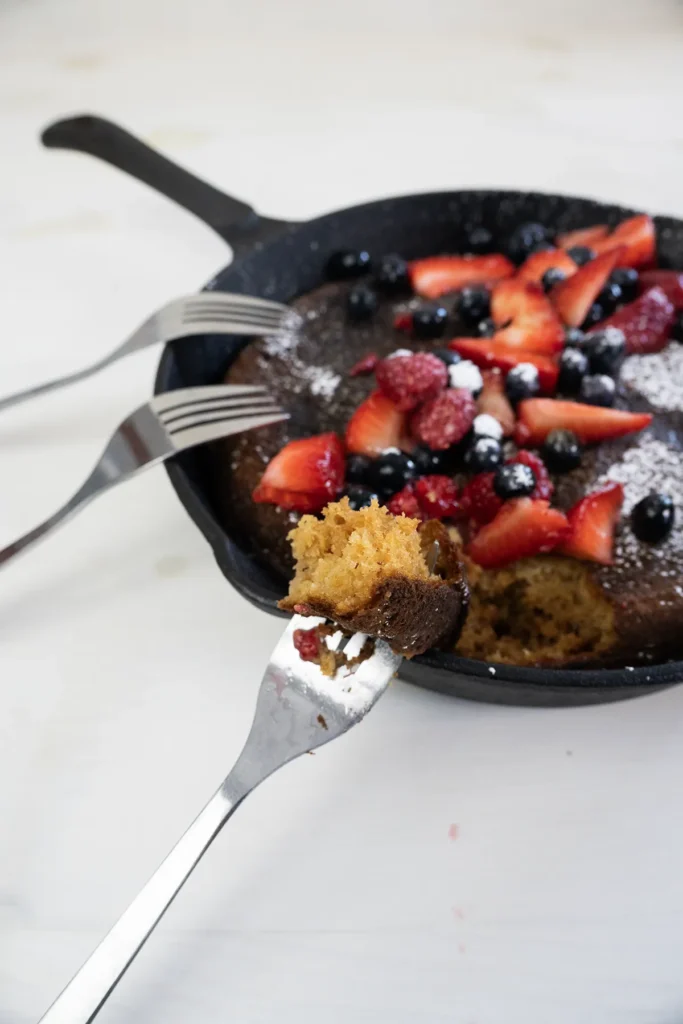 Giant skillet pancake with a group of forks, and a piece of pancake on one of the forks.