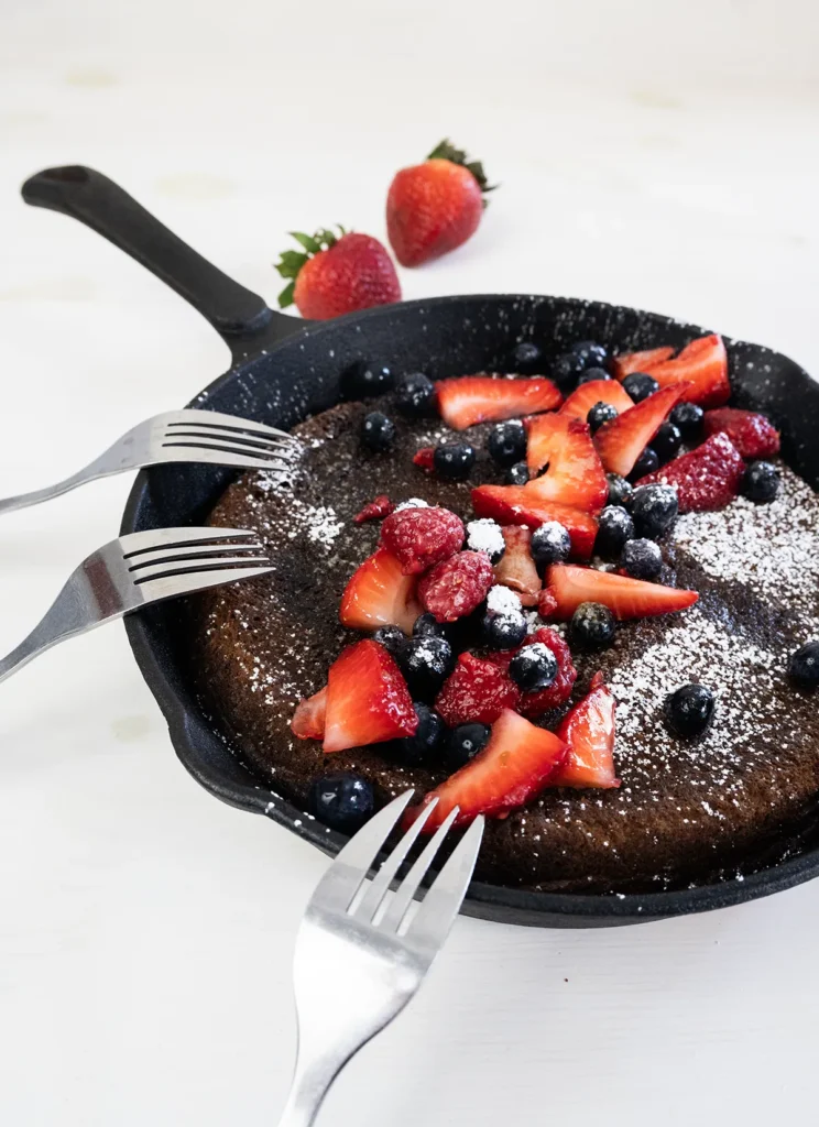 Giant skillet pancake with a group of forks, topped with fresh berries.