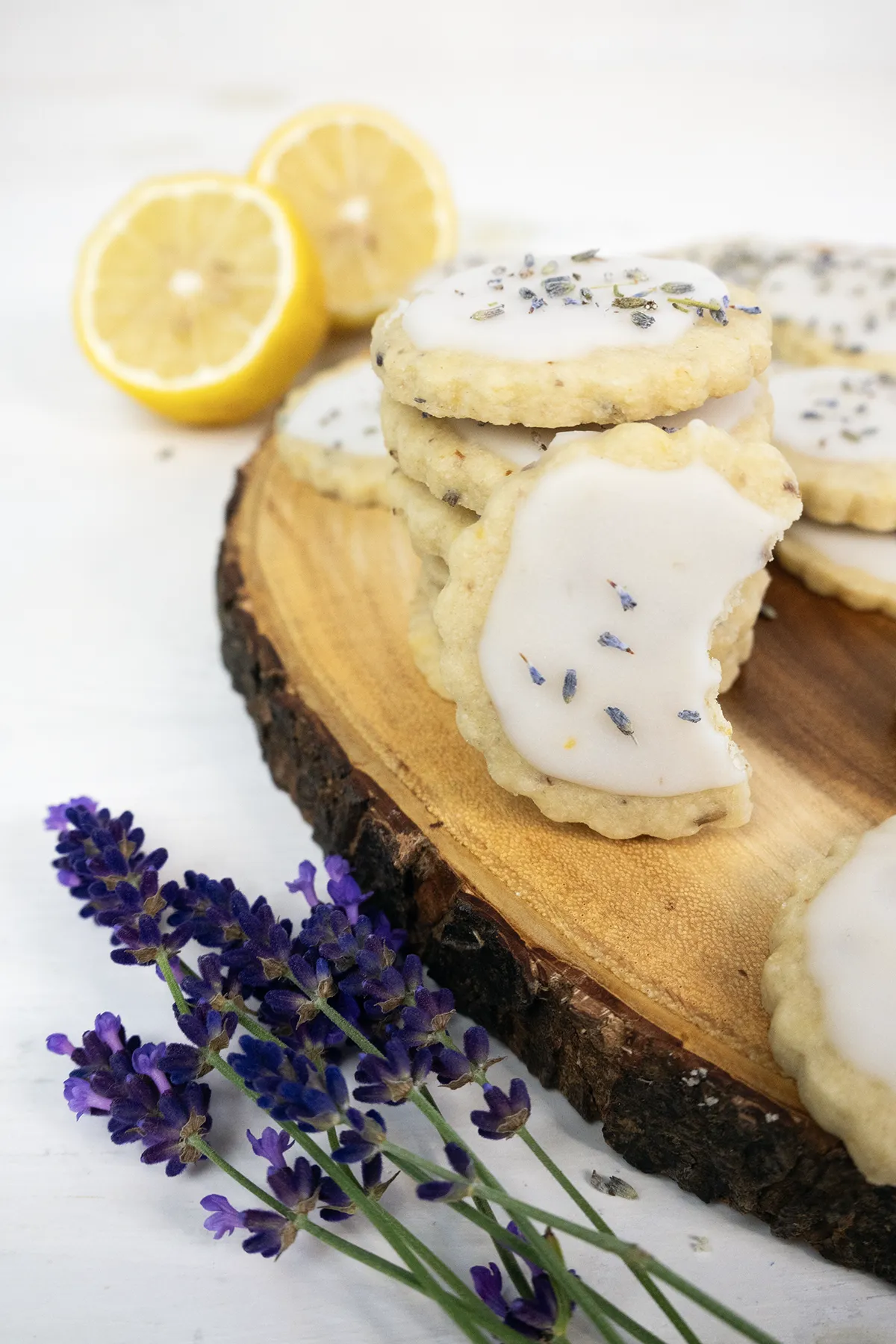 Glazed lemon lavender shortbread cookies stacked on a wooden tray.