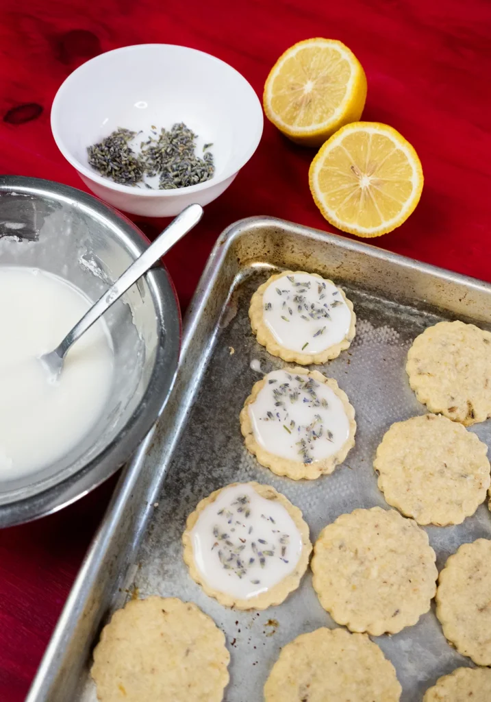 Lemon lavender shortbread cookies on a baking sheet being glazed and decorated with lavender buds.