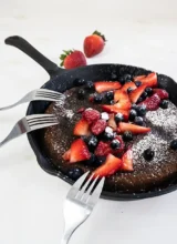 Giant skillet pancake with fresh berries, powdered sugar, and three forks.
