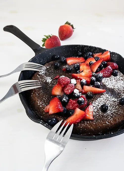 Giant skillet pancake with fresh berries, powdered sugar, and three forks.