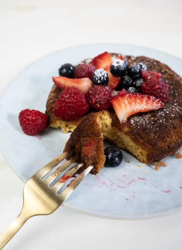 A piece of skillet pancake on a fork rested on the side of a plate, with fresh berries.