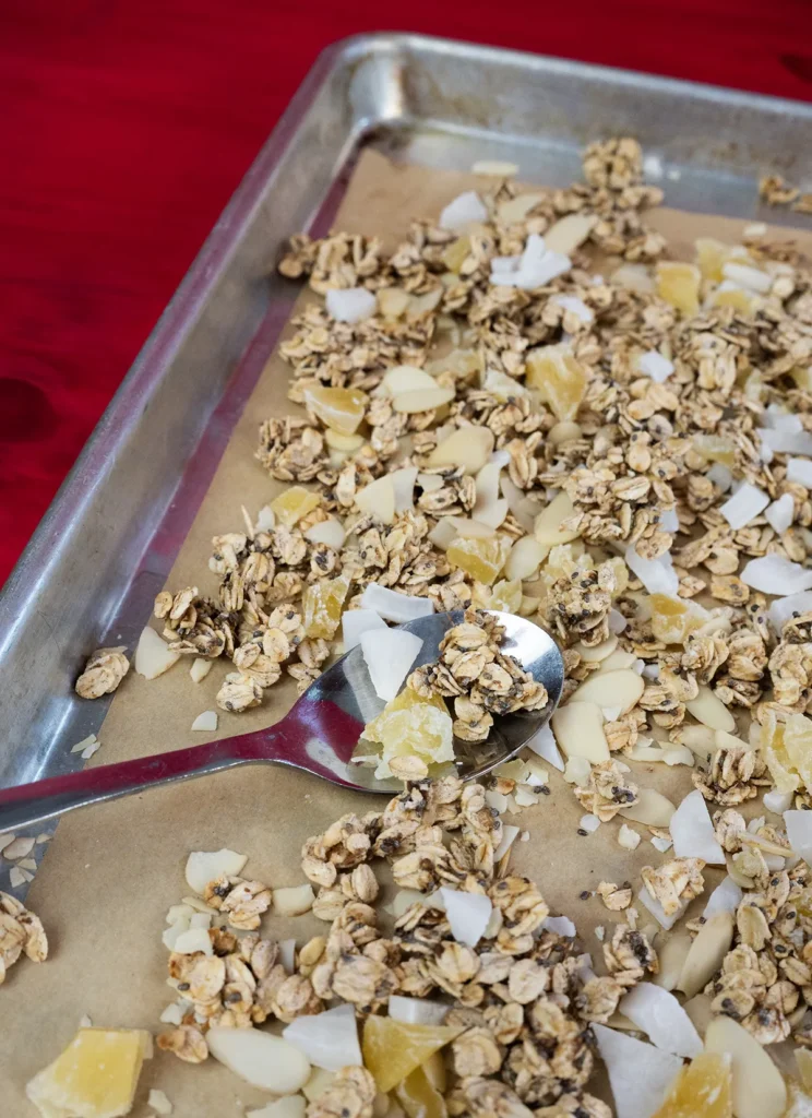 Sourdough granola spread out on a baking sheet with a spoon.