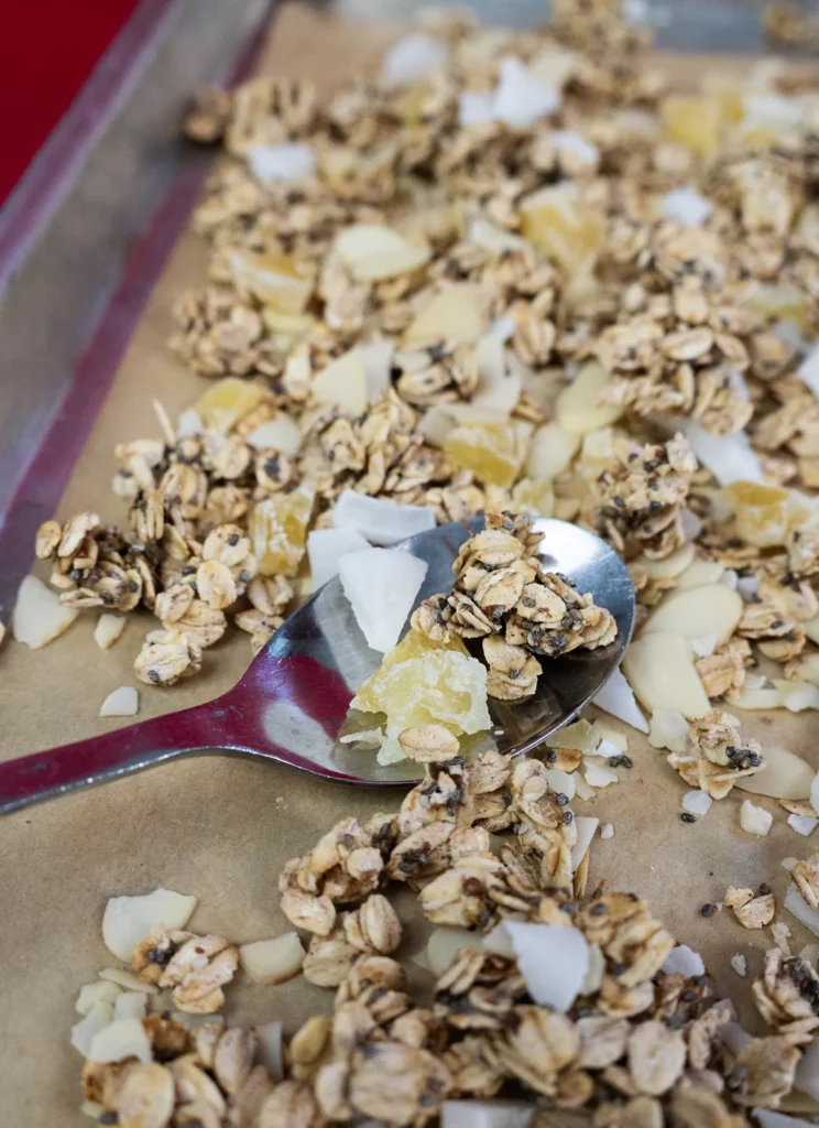 Sourdough granola spread out on a baking sheet with a spoon.