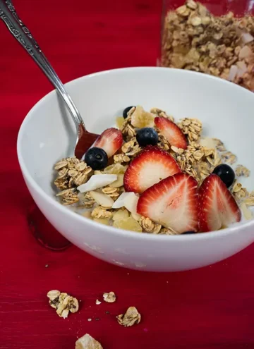 Bowl of sourdough granola topped with fresh strawberries and blueberries.