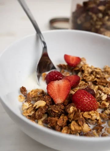 Bowl of sourdough peanut butter granola topped with fresh sliced strawberries.