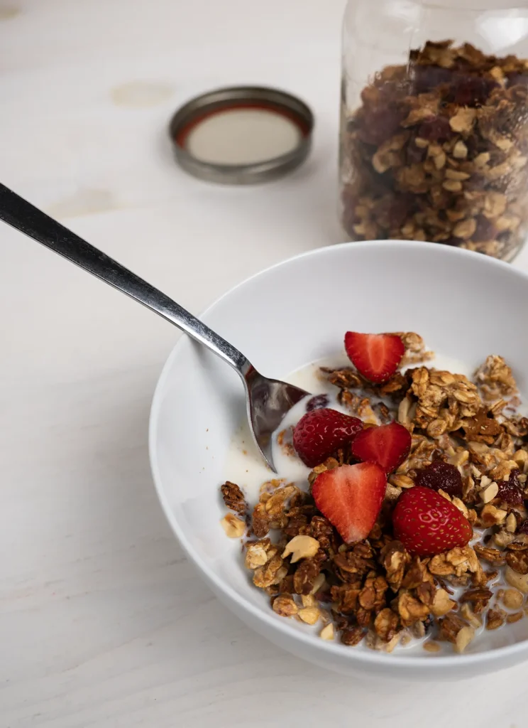 Bowl of sourdough peanut butter granola topped with fresh sliced strawberries.
