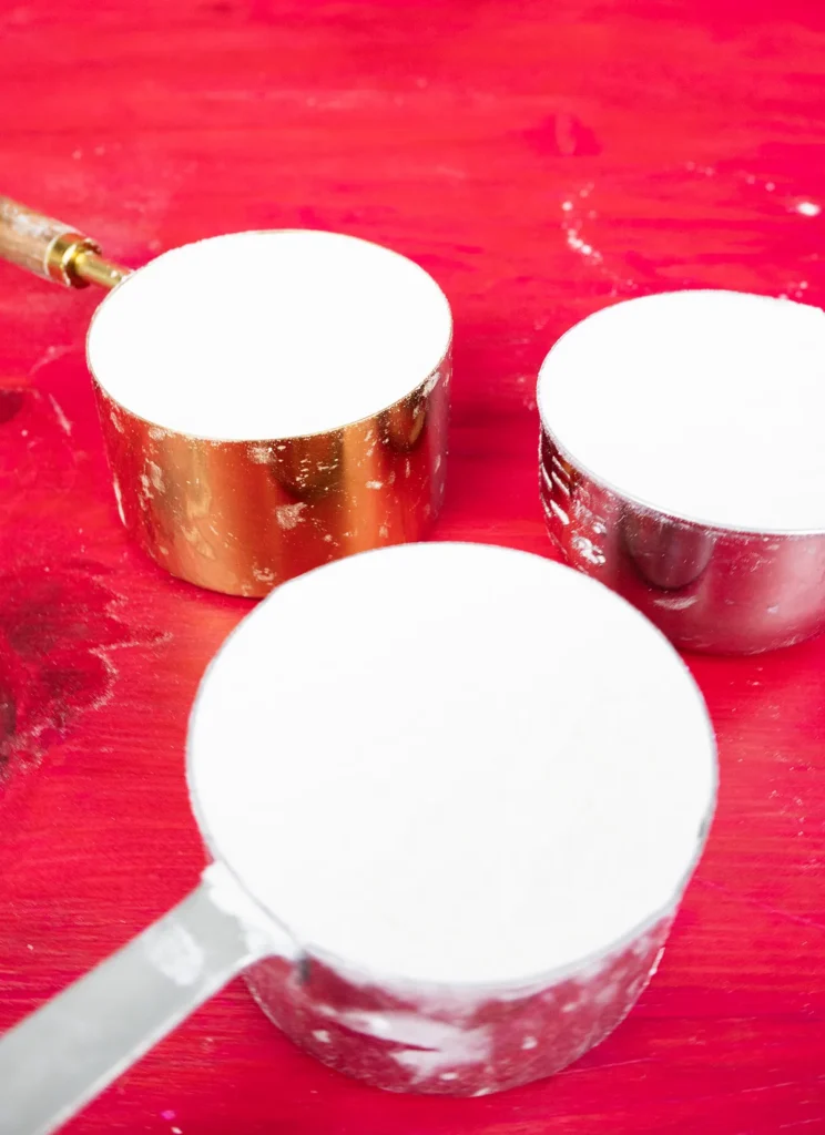 Three cups of flour in a variety of measuring cups.