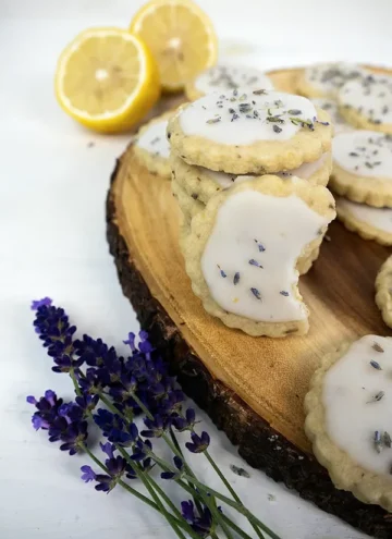 Lemon lavender shortbread cookies arranged on a wooden tray, with lemons and lavender flowers in the background.