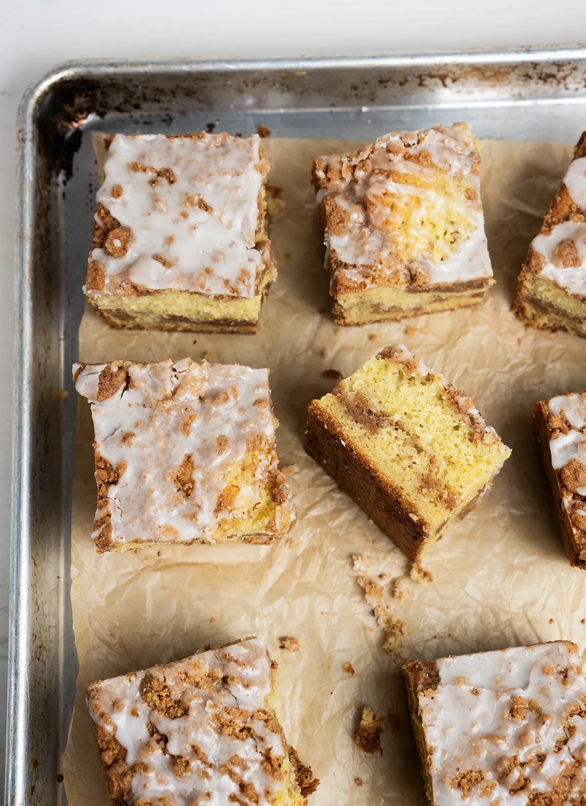 Squares of sourdough discard coffee cake arranged on a parchment-lined baking sheet. One square is on its side, showing off its layers of cake and cinnamon streusel.