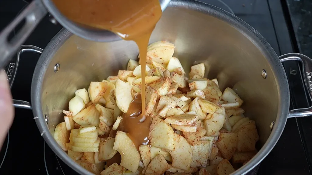 Pouring miso caramel into a pot of chopped apples.