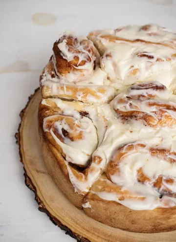 Close-up of cinnamon rolls with cream cheese frosting baked in a round cake pan.