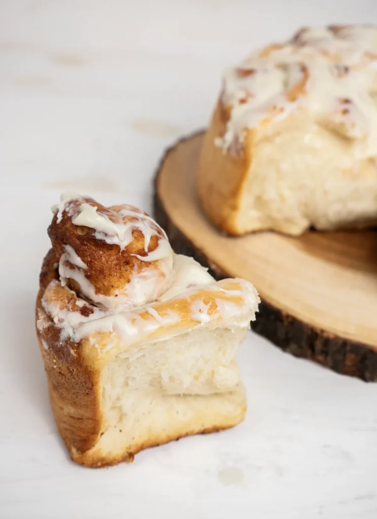 Jumbo cinnamon roll with cream cheese frosting in the foreground, with the rest of the cinnamon rolls in the background on a wooden plate.