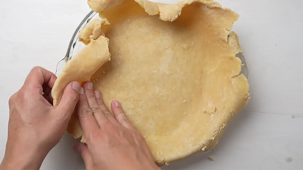 Lining a pie plate with a brown butter pie crust, and pressing it into the corners.