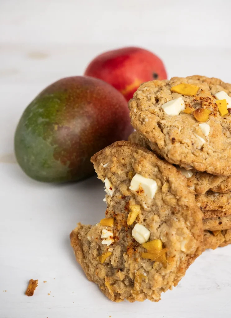 Stack of mango Tajin oatmeal cookies in front of two mangoes.