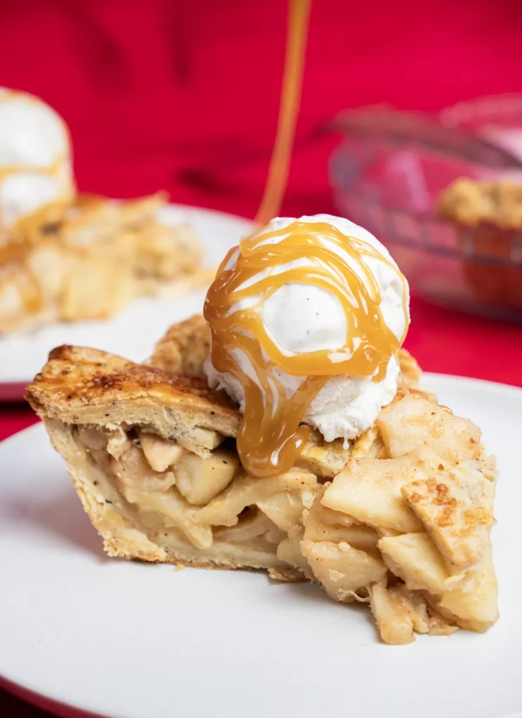 Slice of miso caramel apple pie with a scoop of ice cream, being drizzled with miso caramel.