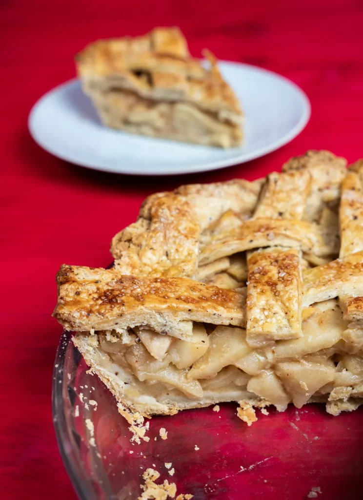 Miso caramel apple pie in a glass pie plate with a slice taken out, and a slice in the background on a plate.
