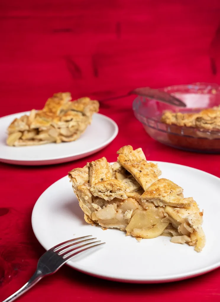 Slices of miso caramel apple pie on plates. A pie plate with the rest of the pie is in the background.