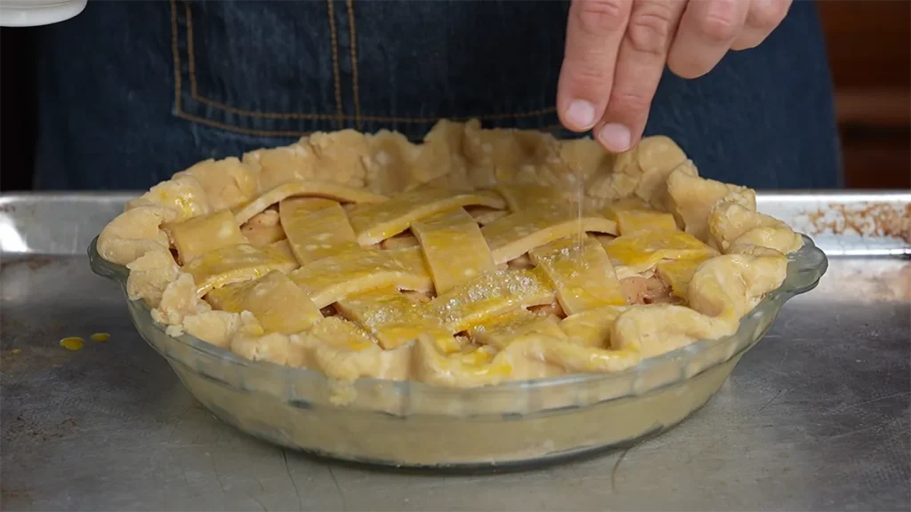 Sprinkling coarse sugar on a lattice crust of a double-crust pie.