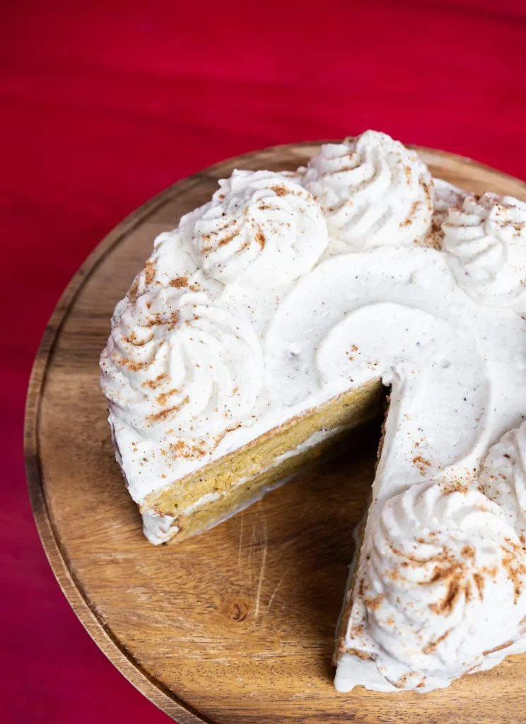 Top view of a pumpkin spice latte tres leches cake on a wooden cake stand, with a slice taken out.