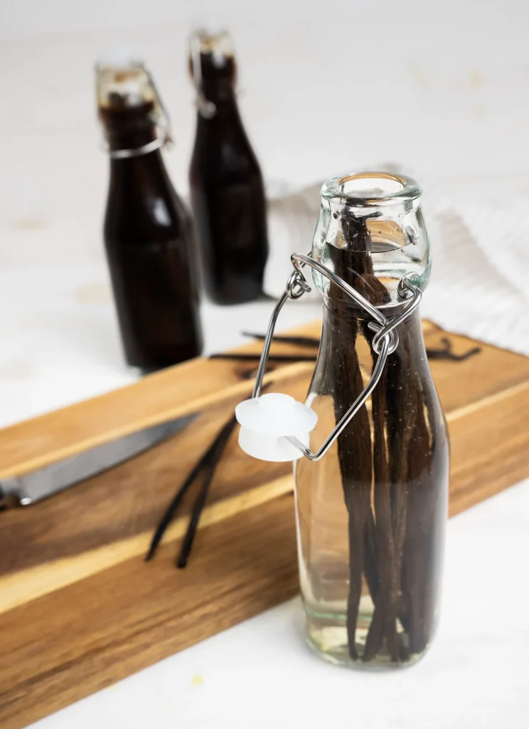 Bottles of vanilla extract, a cutting board, and a vanilla bean being split with a knife.