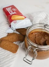 An open jar of homemade cookie butter, an open package of Lotus biscoff cookies and a few scattered biscoff cookies in the background.