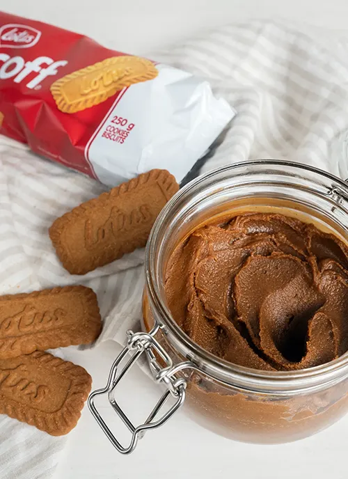 An open jar of homemade cookie butter, an open package of Lotus biscoff cookies and a few scattered biscoff cookies in the background.