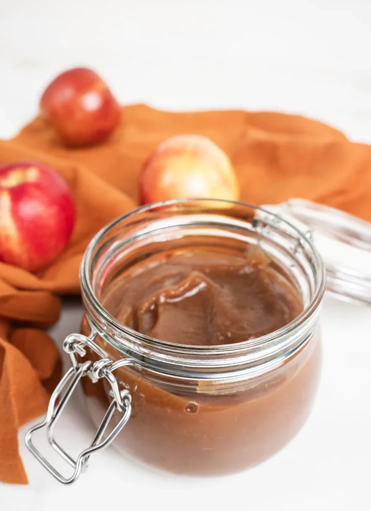 Jar of apple butter with a few apples in the background.
