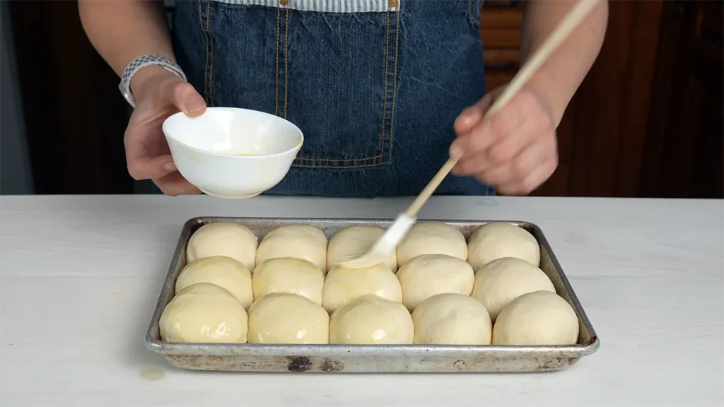 Brushing egg wash onto sourdough Hawaiian rolls ready to be baked.