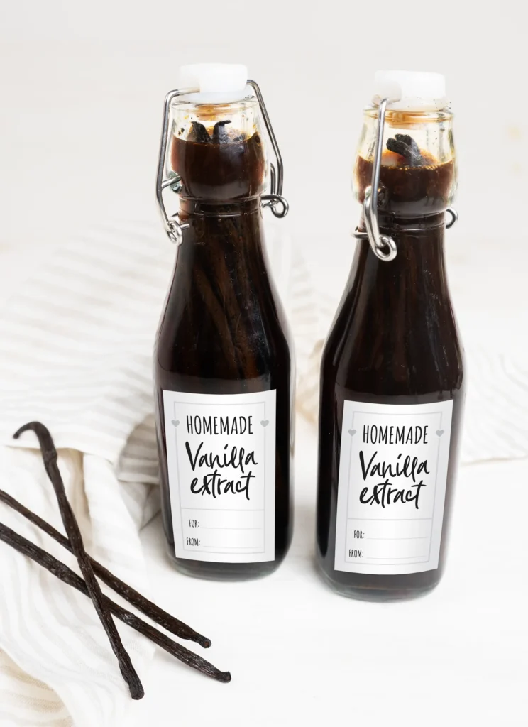 Two bottles of homemade vanilla extract with free printable gift labels. A few vanilla beans in the foreground. 