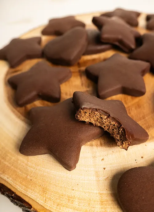 Chocolate-dipped Polish gingerbread (pierniczki) arranged on a wooden plate. One cookie has a bite taken out of it.