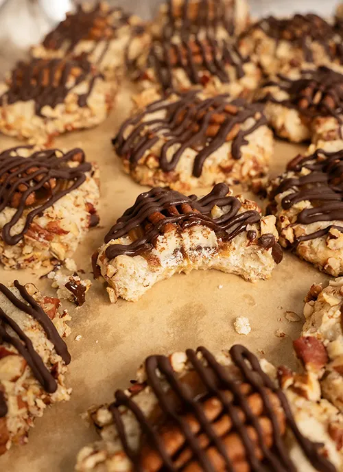 Turtles thumbprint cookies on a sheet of parchment paper. One cookie has a bite taken out of it.