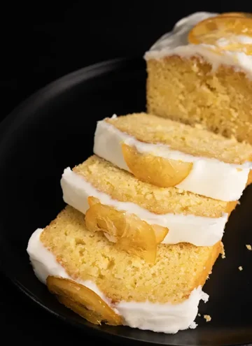 Sliced loaf of velvety-soft lemon pound cake with a luscious thick layer of frosting and candied lemon slices.
