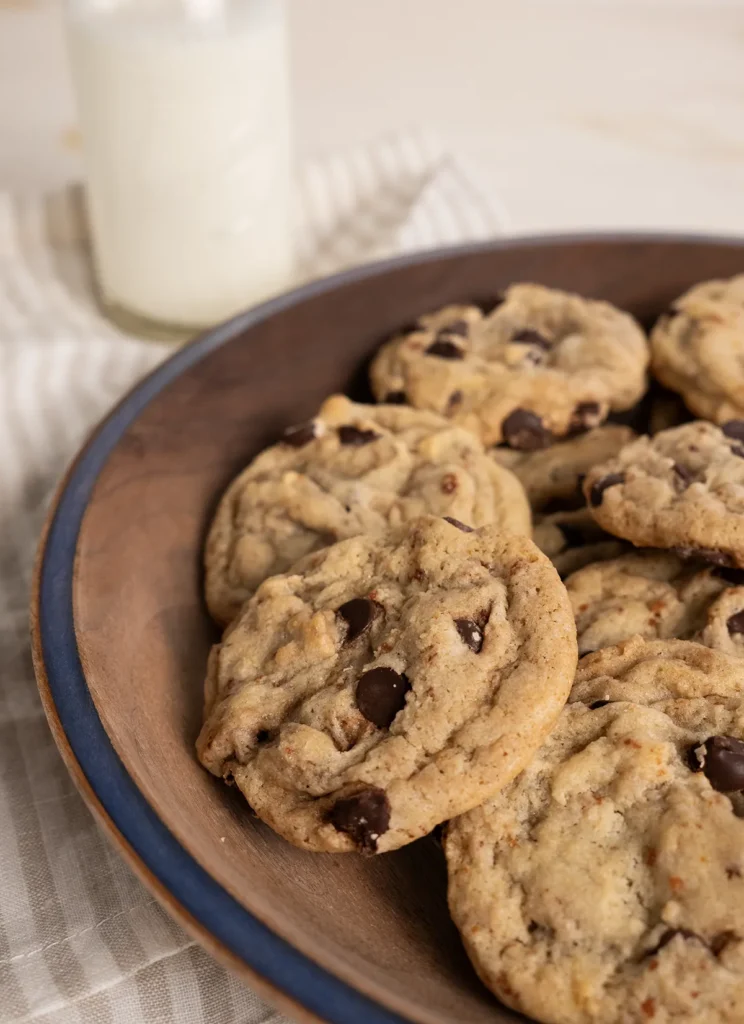 Sourdough chocolate chip cookies on a wooden plate. A bottle of milk is in the background.