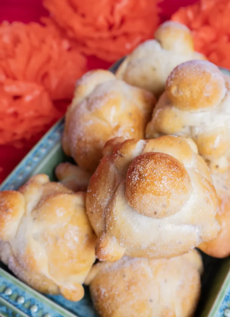 Sourdough Pan de muerto on a wooden board, with orange flowers in the background.