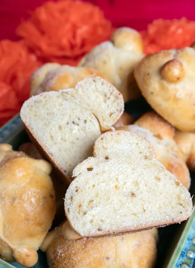 Sourdough Pan de muerto rolls on a black cake stand, with orange flowers in the background.