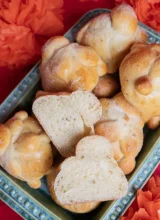 Sourdough Pan de Muerto rolls in a ceramic tray. One is cut open to reveal the pillowy crumb inside.