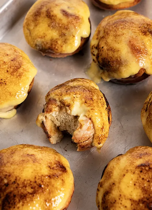Crème Brûlée Cinnamon Rolls on a baking sheet, one roll has a bite taken out of it.