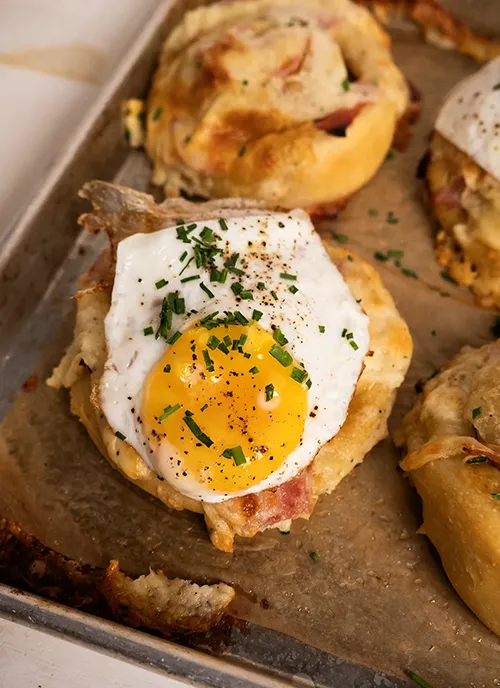 Croque Madame rolls on a baking sheet, sprinkled with chopped chives.