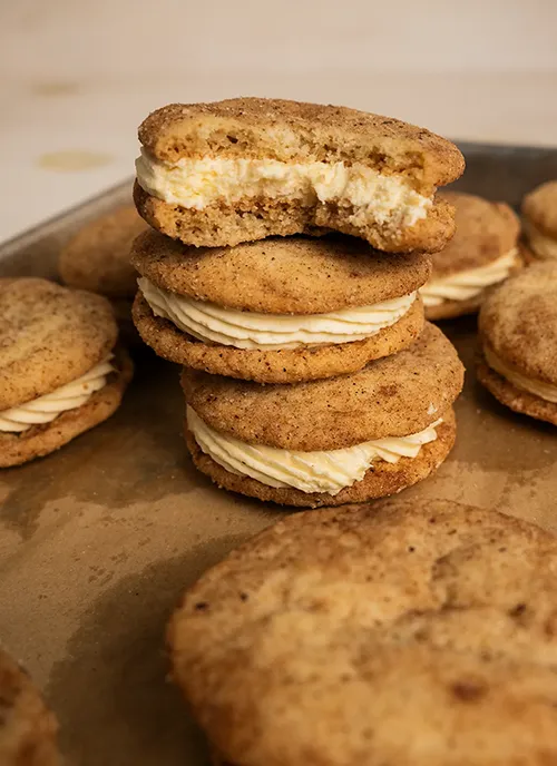 A stack of eggnog snickerdoodle sandwich cookies on a baking sheet. One has a bite taken out of it.