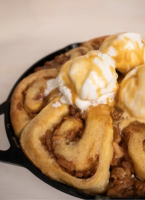 Miso caramel apple pie cinnamon rolls topped with vanilla ice cream and miso caramel.